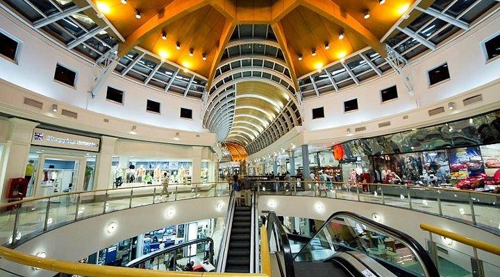 Interior de shopping con escaleras mecánicas y mensaje sobre cine, patio de comidas y promociones.